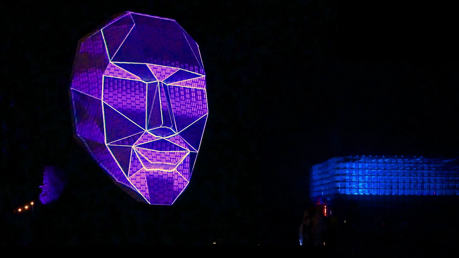 Faceted head sculpture illuminated by purple and pink geometric lines.