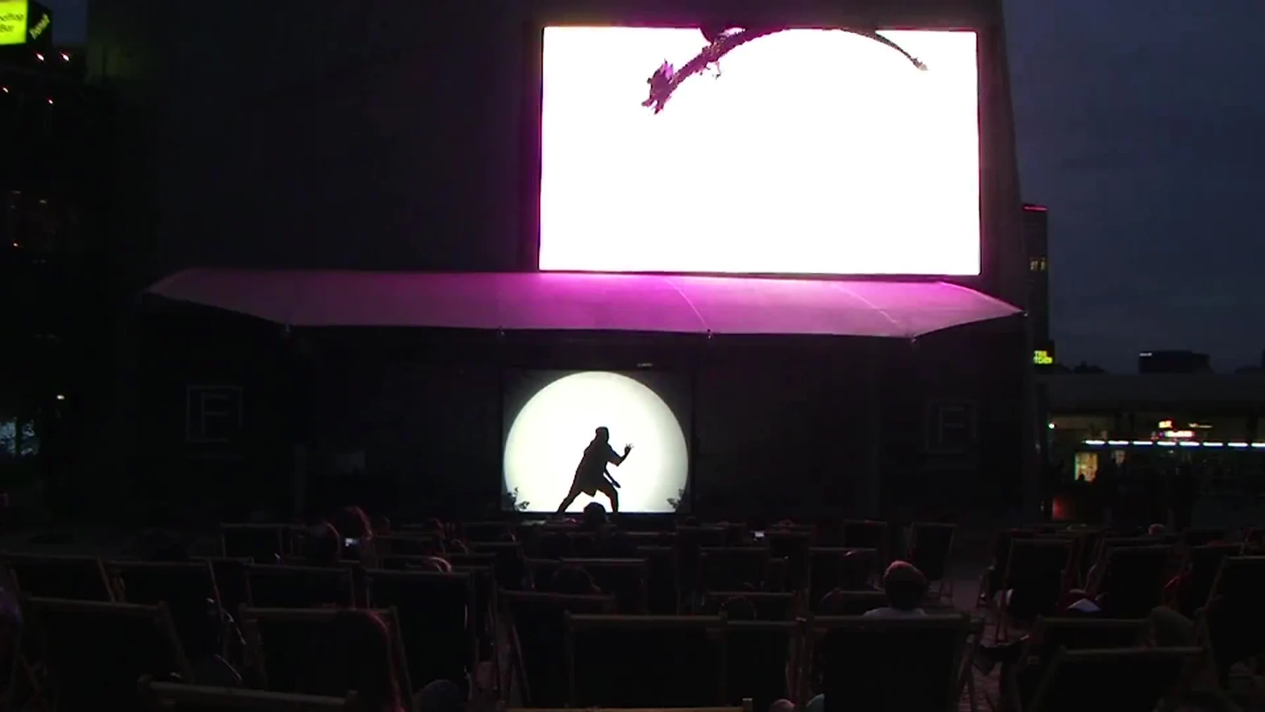 An animated dragon above a performer silhouetted on the Fed Square stage.